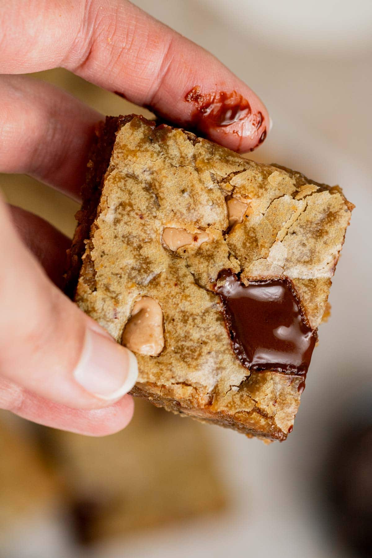 holding brown butter salted caramel blondie slice with chunk of melted chocolate