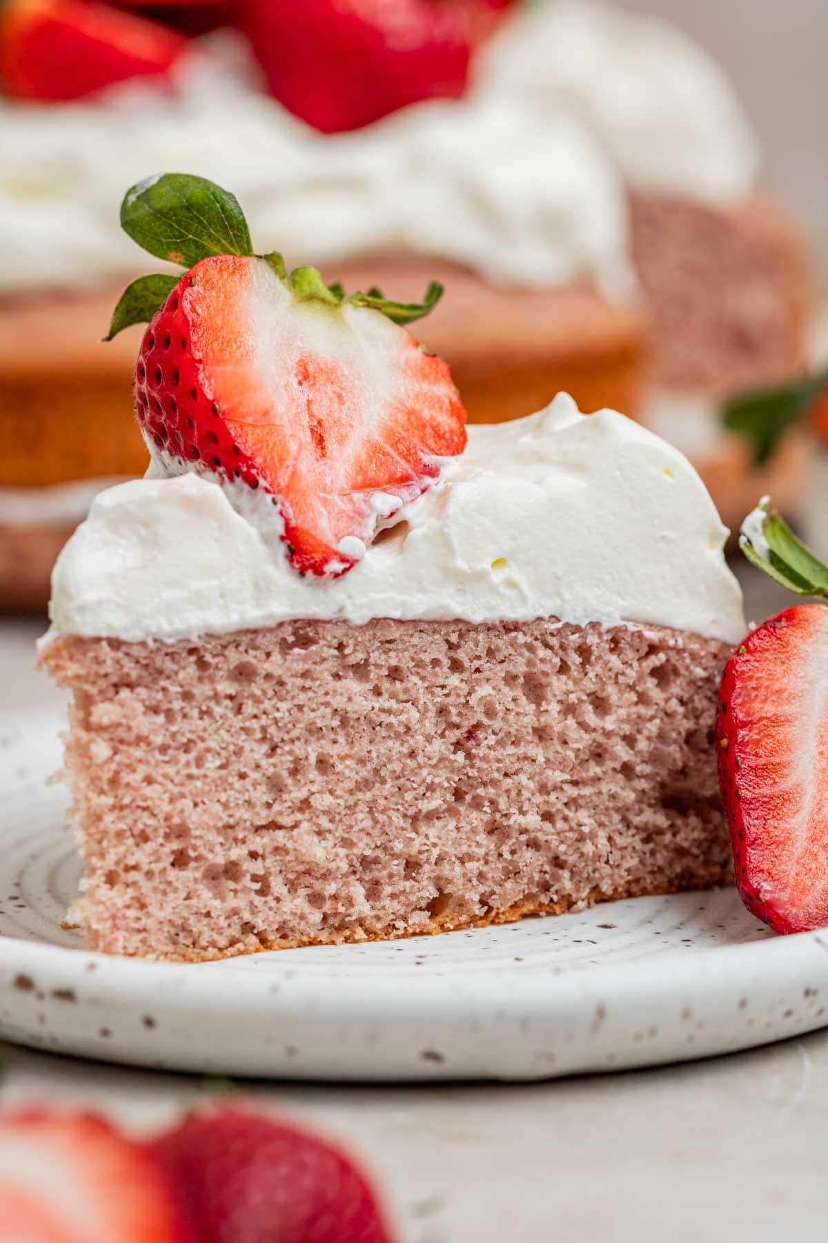 slice of strawberry cake on a plate with fresh strawberries and whipped cream frosting