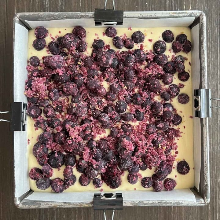A square baking dish filled with blueberries over cheesecake.