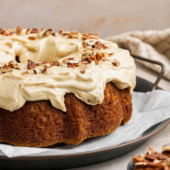close up of carrot bundt cake on a platter slathered in cream cheese frosting