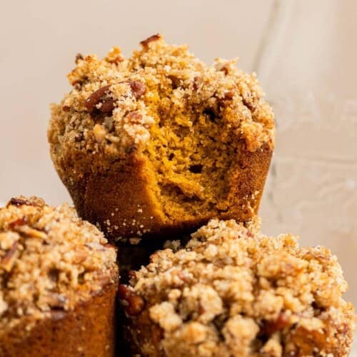 bite taken out of pumpkin muffin sitting on two other pumpkin muffins. All finished with pecan Streusel